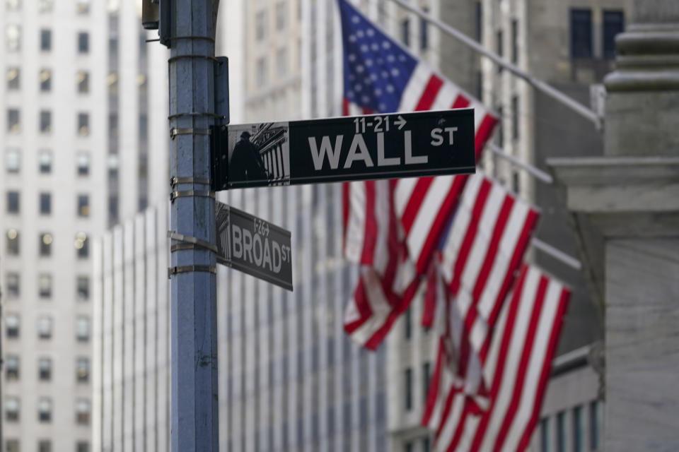 The Wall St. street sign is framed by the American flags flying outside the New York Stock exchange, Friday, Jan. 14, 2022, in the Financial District. Stocks are opening with solid gains on Wall Street Wednesday, Jan. 26, led by technology stocks after Microsoft reported standout results for its latest quarter. (AP Photo/Mary Altaffer)