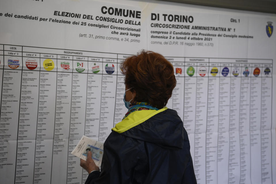 A woman looks at candidates' names and party logos at a polling station in Turin, Italy, Sunday, Oct. 3, 2021. Millions of people in Italy started voting Sunday for new mayors, including in Rome and Milan, in an election widely seen as a test of political alliances before nationwide balloting just over a year away. (Fabio Ferrari/LaPresse via AP)