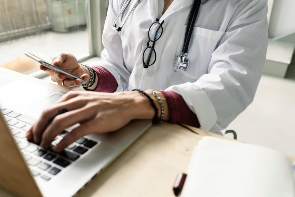 Doctor uses computer an smartphone simultaneously.