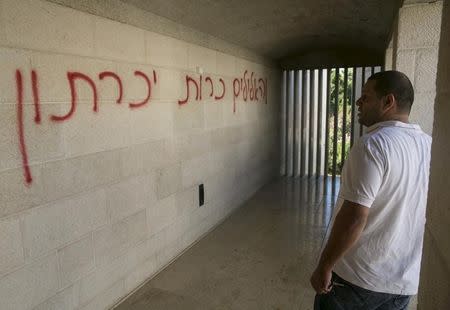 A man looks at graffiti that reads in Hebrew "banish false gods" spray-painted on a wall in the Church of Loaves and Fishes on the shores of the Sea of Galilee in northern Israel June 18, 2015. REUTERS/Baz Ratner