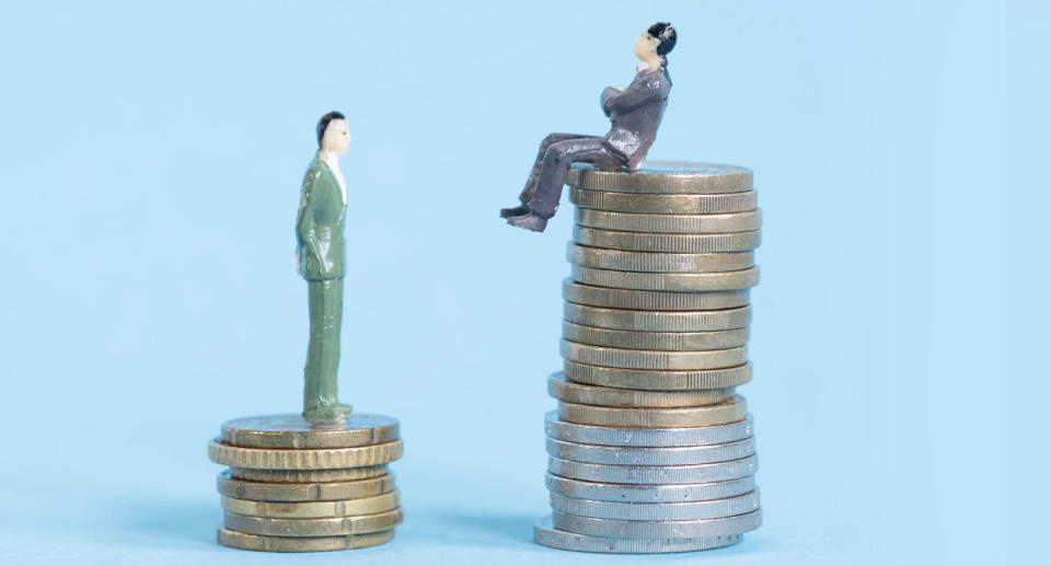 Pay gap represented by to figurines standing on stacks of coins, one larger than the other. 