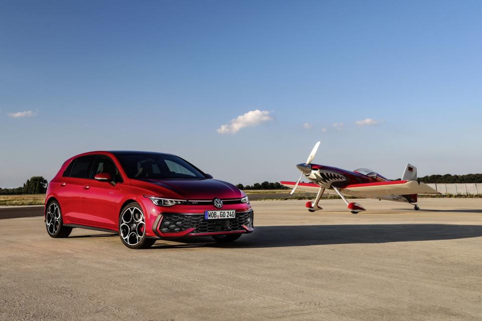 a red car parked next to a small plane