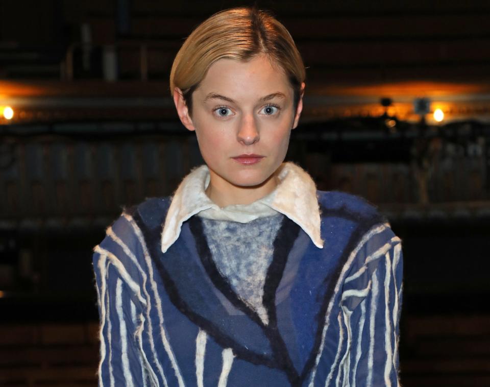 Emma wears a blue sweater with white stripes and collared shirt