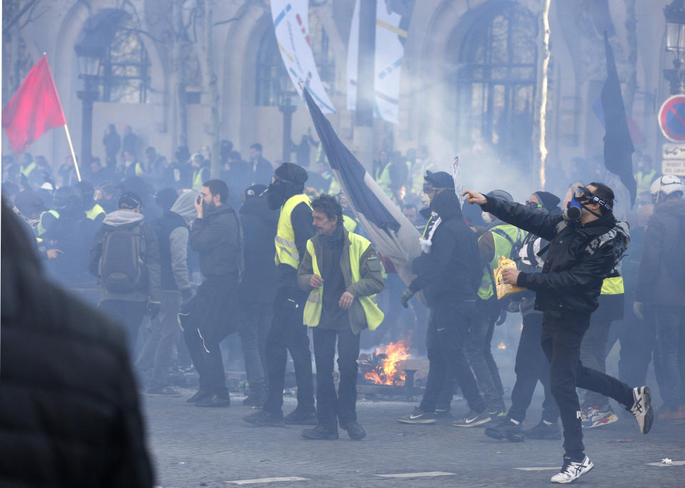 Protesters throw items to police forces during a yellow vests demonstration Saturday, March 16, 2019 in Paris. Paris police say more than 100 people have been arrested amid rioting in the French capital by yellow vest protesters and clashes with police. They set life-threatening fires, smashed up luxury stores and clashed with police firing tear gas and water cannon (AP Photo/Christophe Ena)