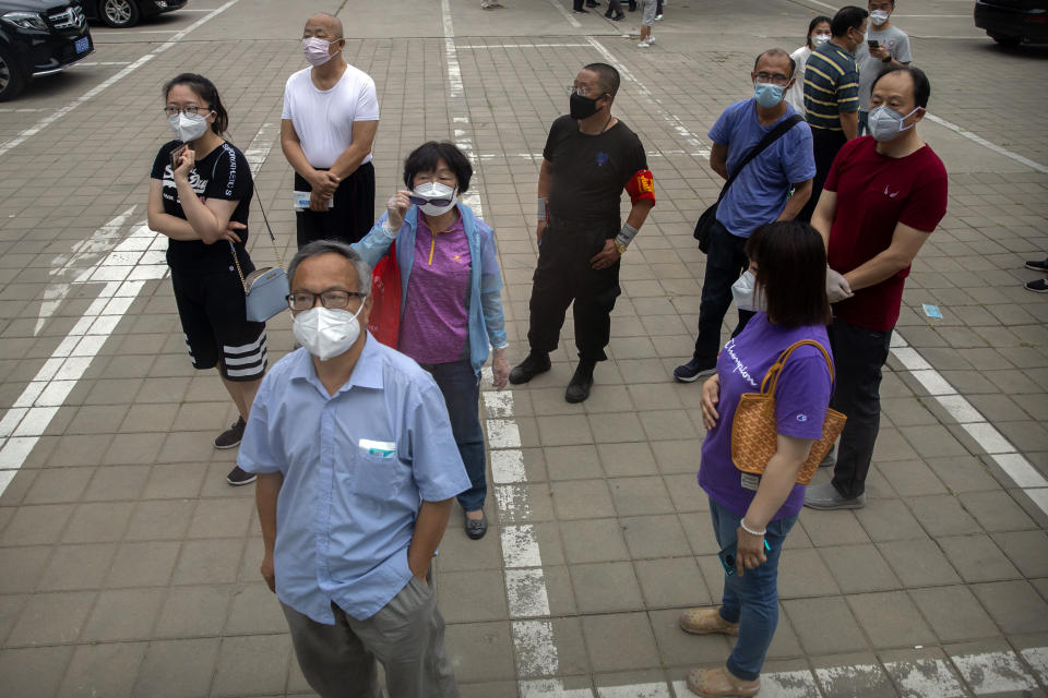 People wearing face masks watch as a bus of tested patients leaves a COVID-19 testing site for those who were potentially exposed to the coronavirus outbreak at a wholesale food market in Beijing, Wednesday, June 17, 2020. As the number of cases of COVID-19 in Beijing climbed in recent days following an outbreak linked to a wholesale food market, officials announced they had identified hundreds of thousands of people who needed to be tested for the coronavirus. (AP Photo/Mark Schiefelbein)