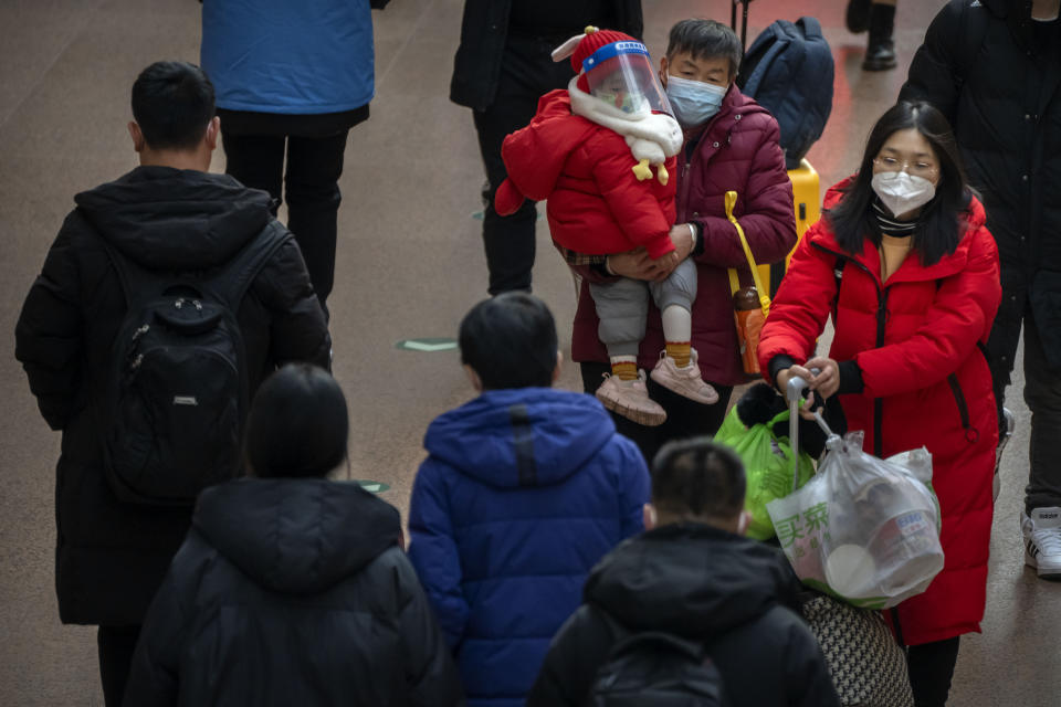 A woman carries a child wearing a face mask and face shield as they walk along a concourse at Beijing West Railway Station in Beijing, Wednesday, Jan. 18, 2023. China in December lifted its strict "zero-COVID" policy, letting loose a wave of pent-up travel desire, particularly around China's most important time for family gatherings, referred to in China as the Spring Festival, that may be the only time in the year when urban workers return to their hometowns. (AP Photo/Mark Schiefelbein)