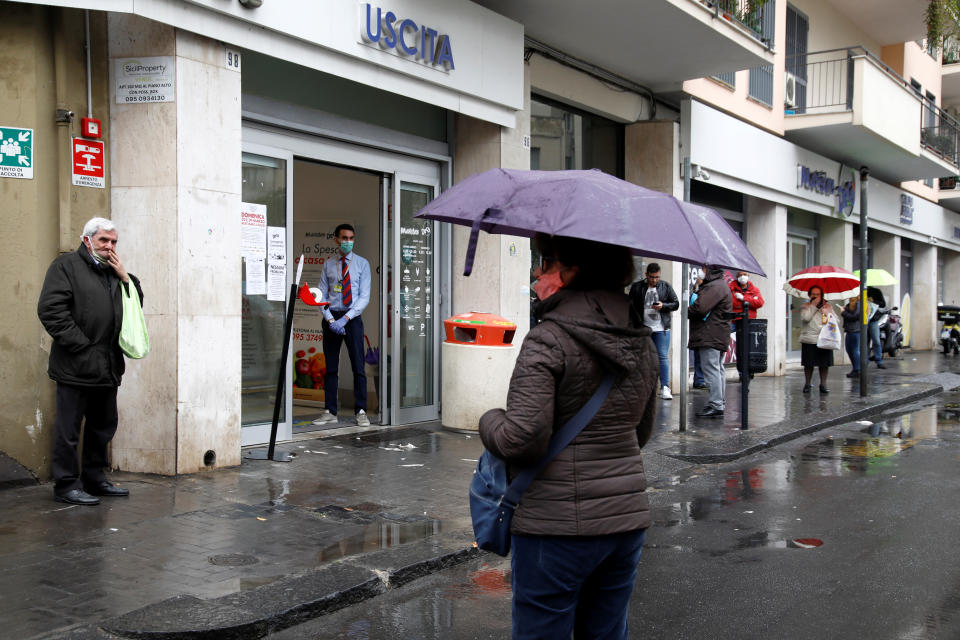 People line up in the rain outside a supermarket after the Italian island of Sicily closed them on Sunday, as it tightens measures to try and contain the spread of coronavirus disease (COVID-19), in Catania, Italy March 23, 2020. REUTERS/Antonio Parrinello