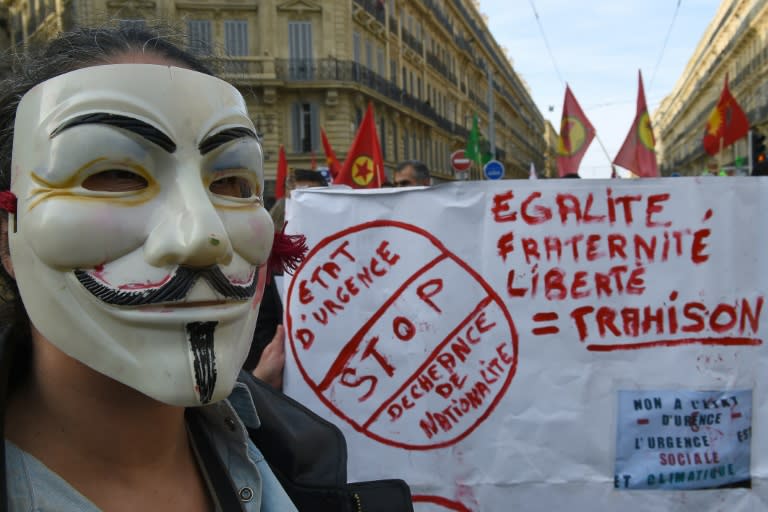 A person wearing a Guy Fawkes mask stands next to a banner reading "Stop the state of emergency and the loss of nationality" during a demonstration in Marseille, southern France, on January 30, 2016