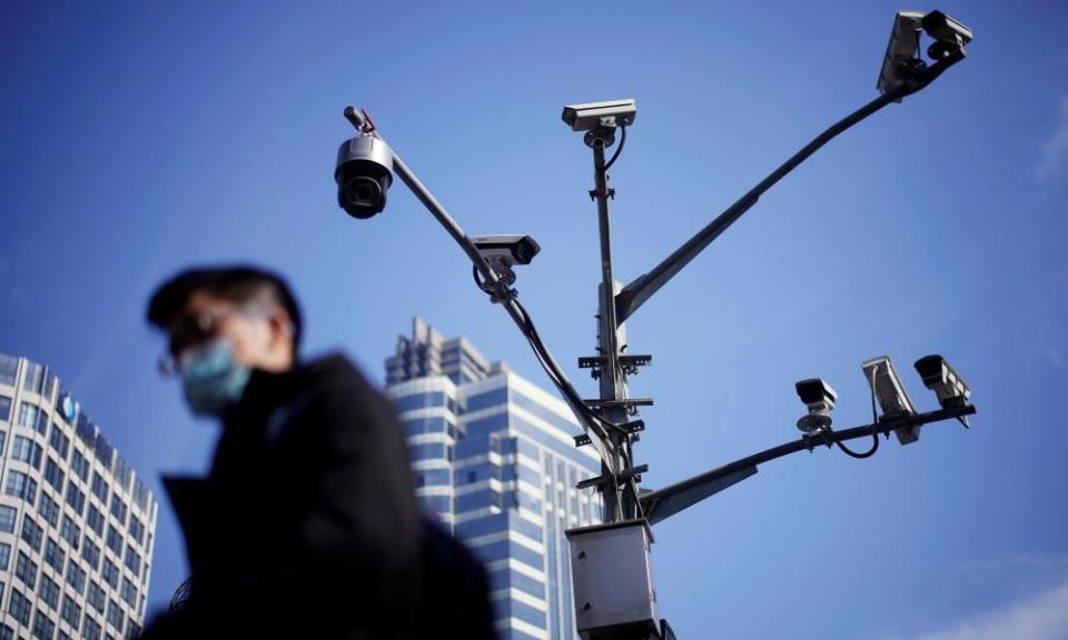 A man in a mask shot from below, with a tall multi-branched camera mast rising above him in the street