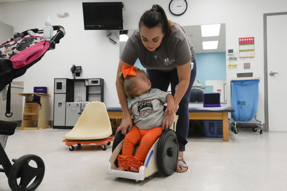 Heather Hampton helps her daughter Freya Baudoin, 18 months, into her new mobility chair at the Children's Hospital New Orleans Rehabilitation Center in Metairie, La., Monday, Oct. 30, 2023. Tulane science and engineering students are making the second batch of mobility chairs for toddlers, that will eventually go to pediatric patients at Children's Hospital. Wheelchairs are expensive, and insurance won't cover the cost for children unless the child proves they can operate it independently. (AP Photo/Gerald Herbert)
