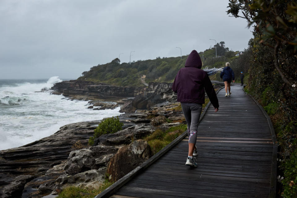 A woman walks in strong winds and rainy conditions at South Curl Curl Beach on October 26 in Sydney. Source: Getty