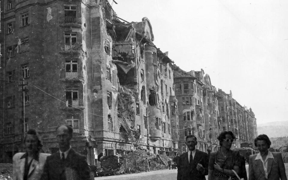 Circa 1945: People walk past bombed-out buildings from the Allied liberation of Hungary, Budapest