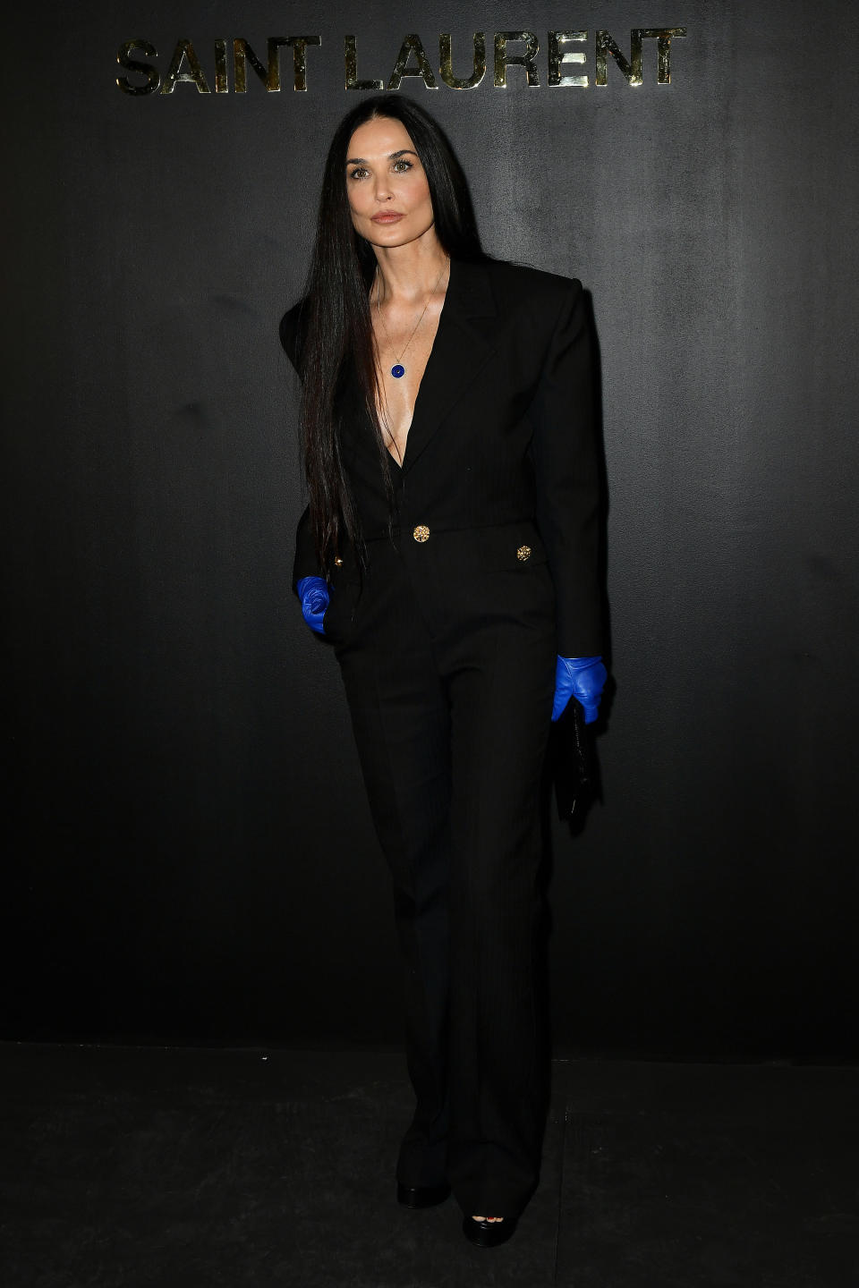 Demi Moore attends the Saint-Laurent Womenswear Fall/Winter 2022/2023. She wears a black suit with a plunging neckline and electric blue leather gloves.