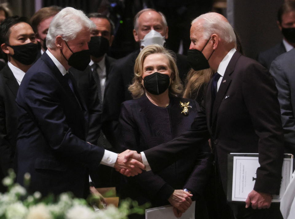 Former President Bill Clinton shakes President Biden's hand as former Secretary of State Hillary Clinton looks on.