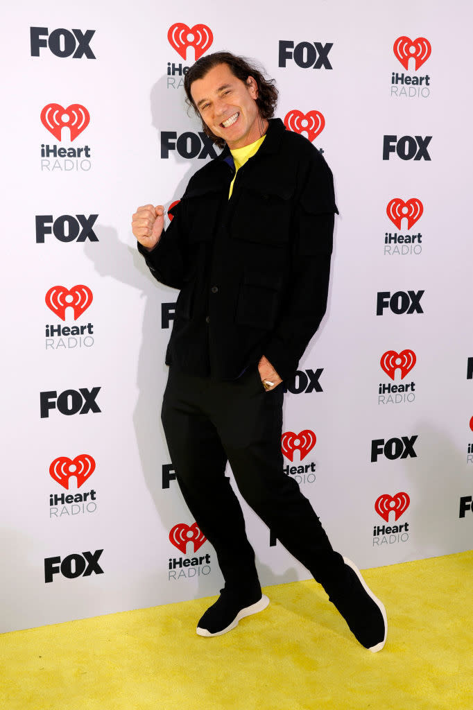 Man in a black outfit with yellow highlights poses with a thumbs-up on a media event backdrop