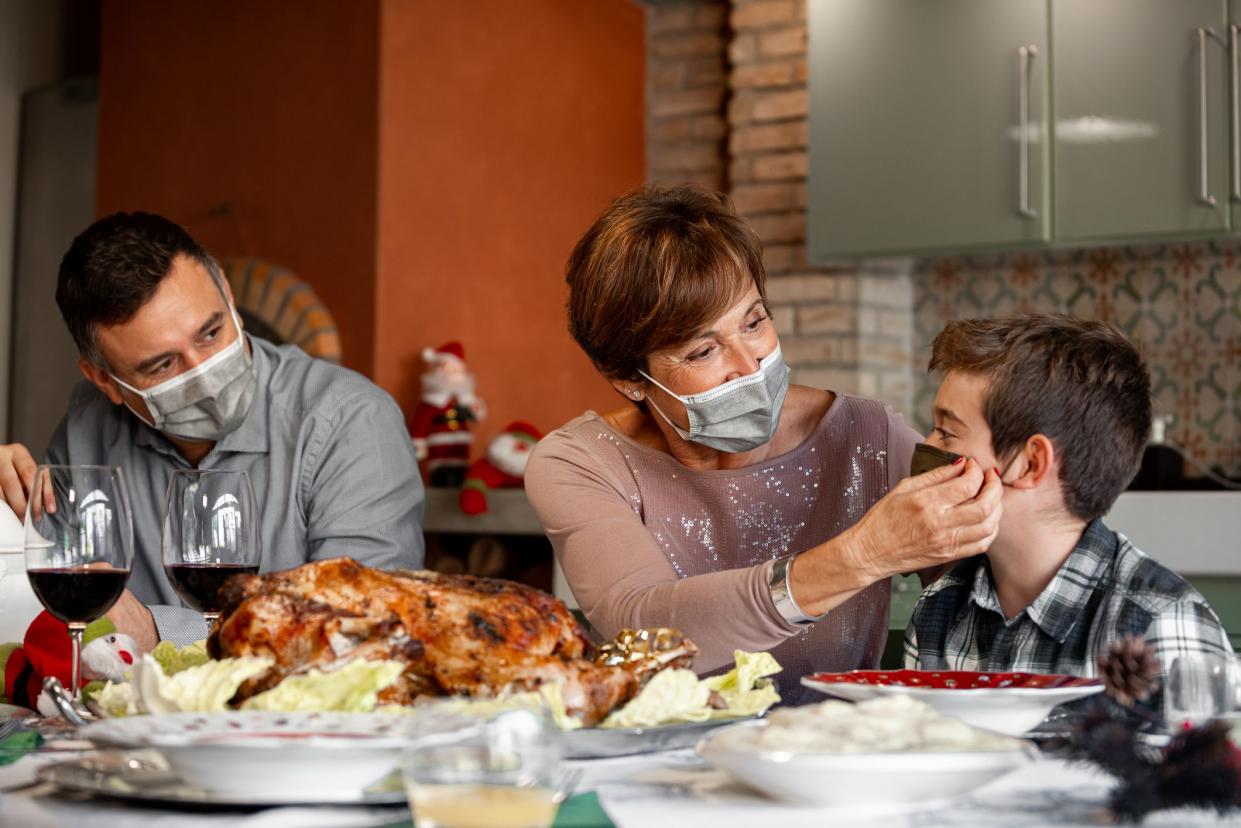 Family sitting at the Christmas Thanksgiving table at home in the year of the Coronavirus Pandemic. Grandmother adjust the surgical mask to her grandson. New rules, Covid outbreak, lockdown.