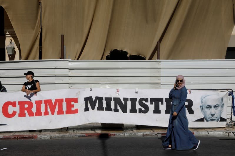 FILE PHOTO: A woman walks past a banner depicting Israeli PM Netanyahu and words "Crime Minister" outside the Justice Ministry in Jerusalem