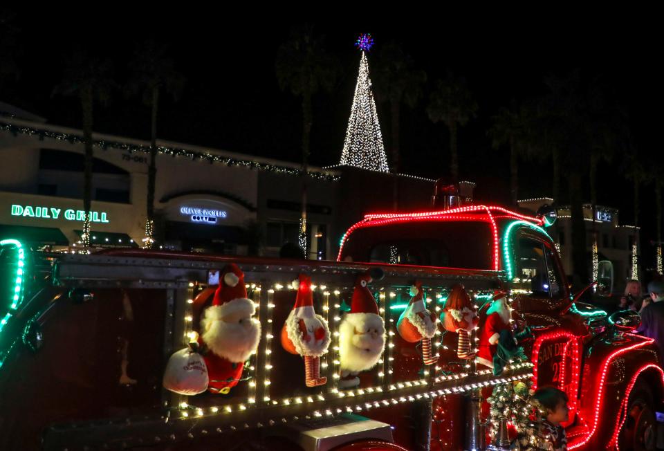 A rooftop Christmas tree of lights is seen lit up in the distance behind a vintage firetruck decorated for the holidays at the El Paseo Shopping District, Friday, Dec. 3, 2021, in Palm Desert, Calif. 