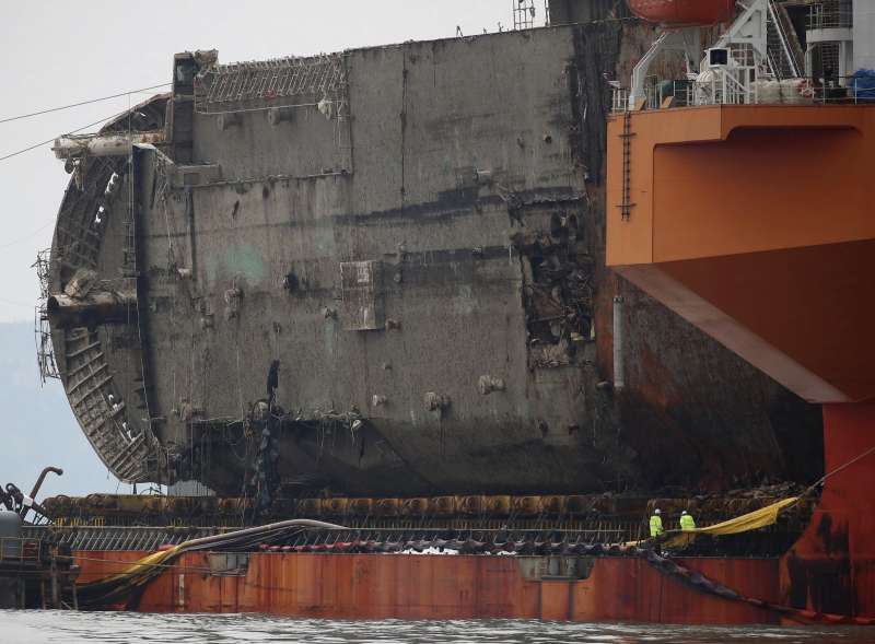 2014年4月沉沒、奪走304條人命的南韓渡輪「世越號」26日被抬到半潛船上，準備運往木浦新港（AP）