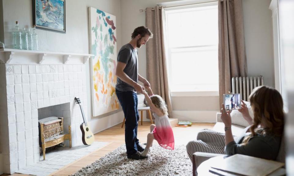 Mother videoing father and daughter dancing in living room