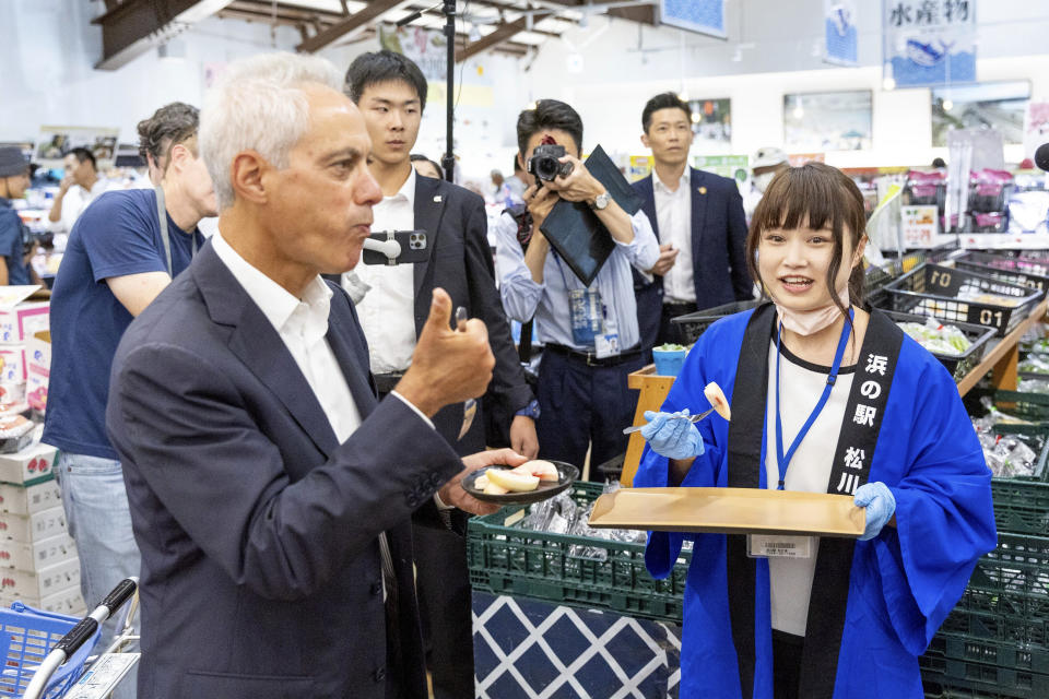 In this photo provided by U.S. Embassy, U.S. Ambassador to Japan Rahm Emanuel, left, eats peach samples at a market in Soma city, Fukushima prefecture, Thursday, Aug. 31, 2023. U.S. Ambassador Emanuel visited a northern Fukushima city Thursday and had seafood lunch with the mayor, talked to fishermen and stocked up on local produce at a grocery store to show they're all safe after the release of treated radioactive wastewater from the wrecked Fukushima Daiichi plant to the sea, backing Japan effort while criticizing China's ban on Japanese seafood as political.(U.S. Embassy via AP)