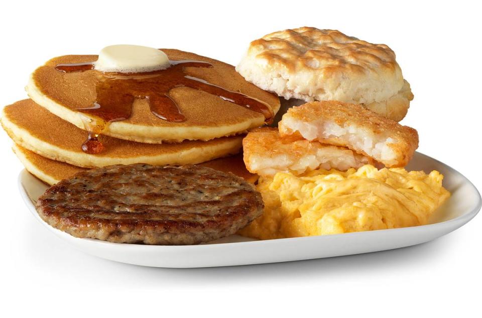The Big Breakfast with hotcakes is a plate piled with pancakes, a biscuit, sausage, scrambled eggs, crispy hash browns and butter and maple syrup.