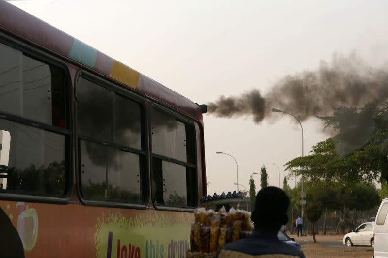 FILE PHOTO: A man sells plantain chips near a bus with smoke seen from its exhaust at a bus park in Abuja