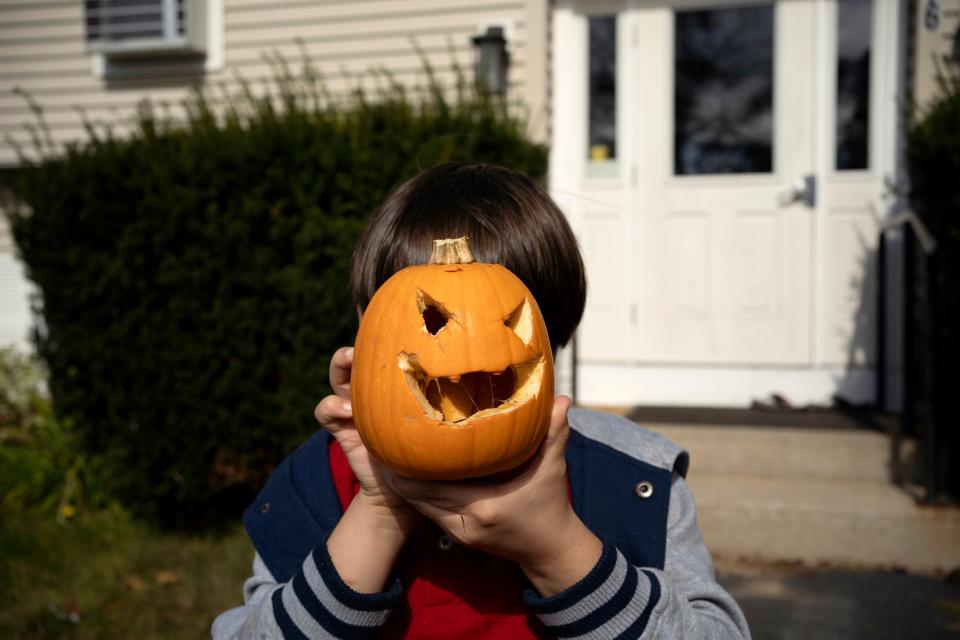 A child holds a carved pumpkin in front of his face.