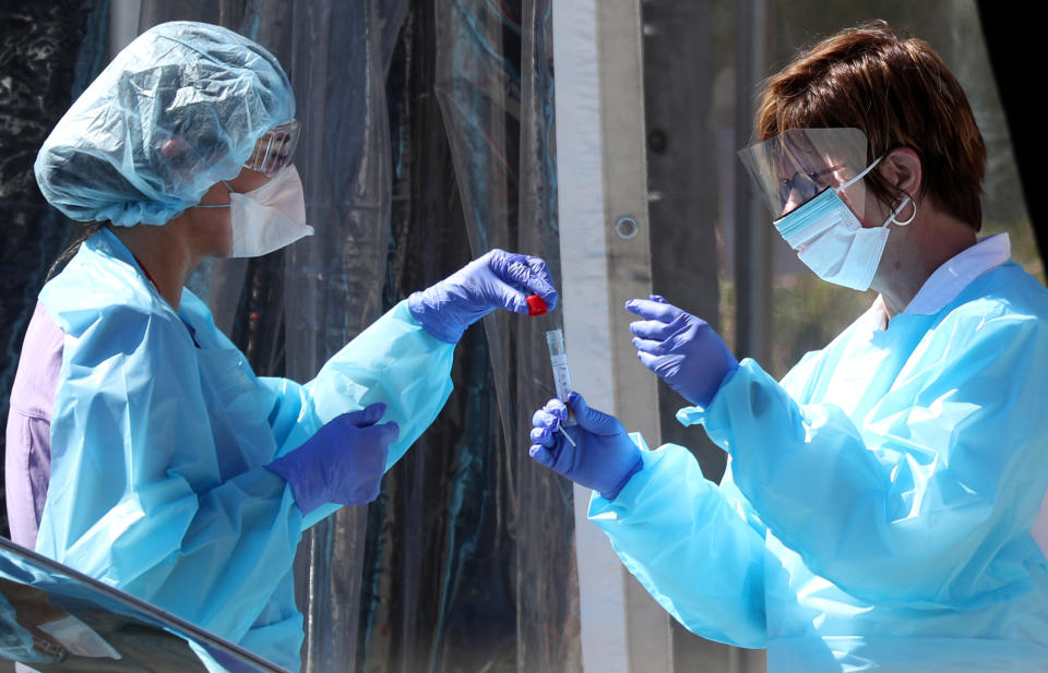 Two medical personnel handle a plastic tube containing a sample at a drive-through COVID testing station.