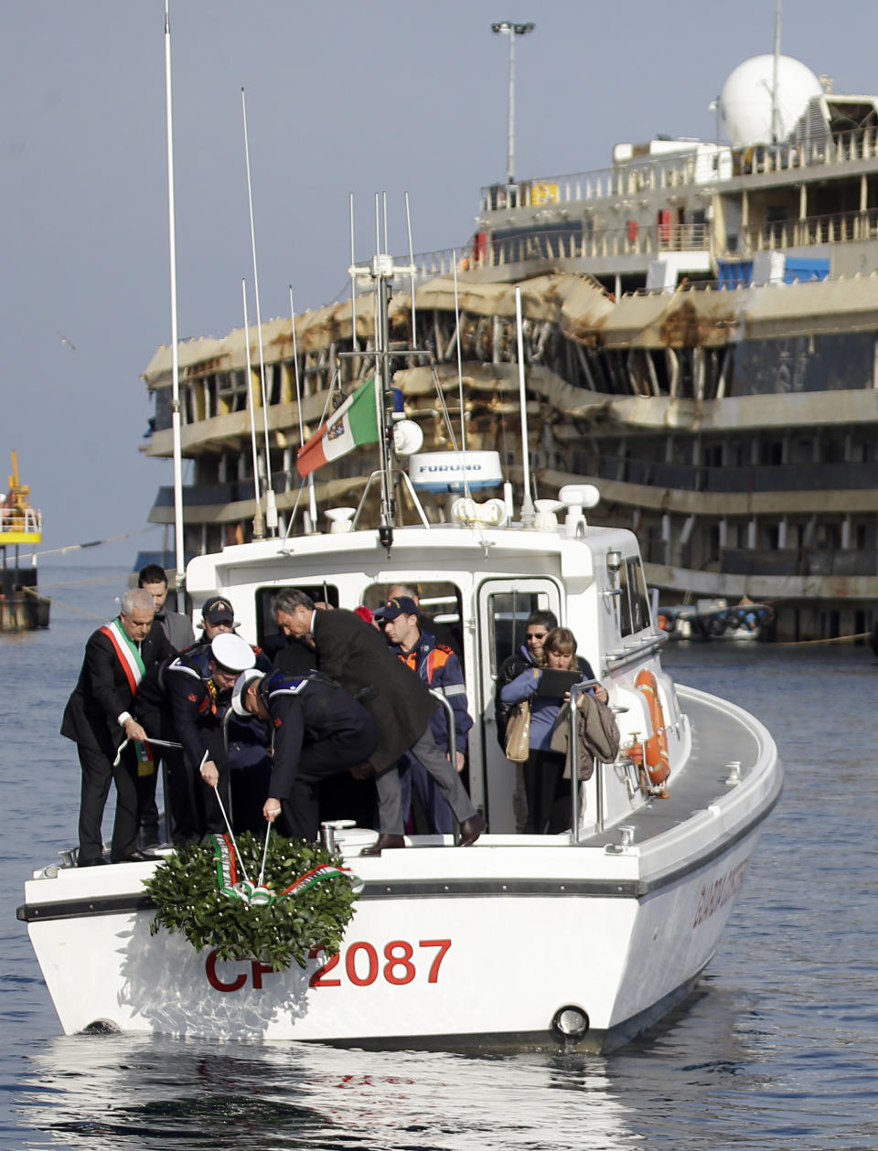 A wreath is being lowered into the water by Italian Navy personnel near the Costa Concordia near the shipwrecked Costa Concordia off the coast of the Tuscan Island of Giglio, Italy, Monday, Jan. 13, 2014. Survivors of the capsized Costa Concordia are commemorating the second anniversary of the grounding off Tuscany that killed 32 people with a candlelight march on the island later on and a moment of silence in the Italian courtroom where the captain is on trial. (AP Photo/Gregorio Borgia)