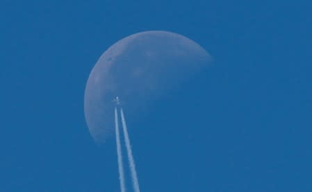 A passenger plane flies in the sky as the Moon is seen in Berlin