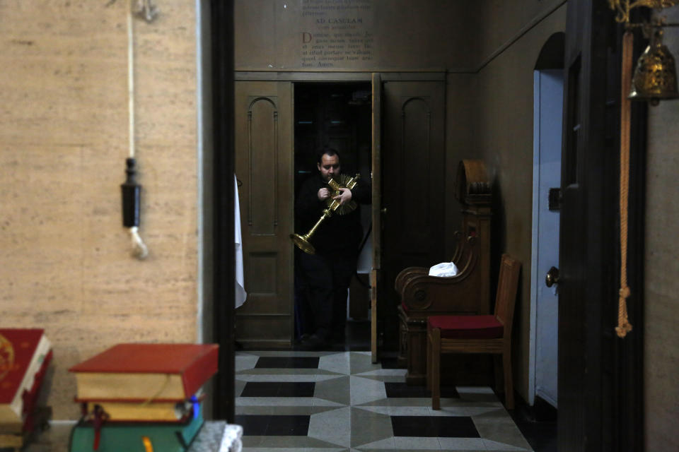 In this April 19, 2020, photo, the Rev. Joseph Dutan prepares for a virtual holy hour livestreamed for the parishioners of St. Brigid Church in the Brooklyn borough of New York. The harm caused by the coronavirus is all around him: The funeral home across from St. Brigid, always busy. (AP Photo/Jessie Wardarski)