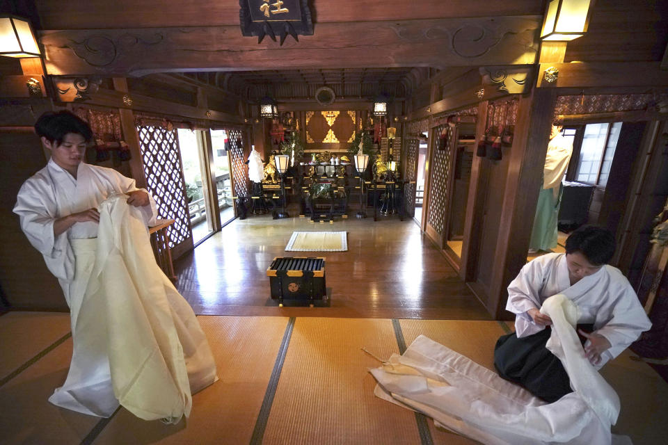 In this May 8, 2020, photo, priests put ritual dress away after performing a livestream prayer during a 10-day trial of "online shrine" visit program at Onoterusaki Shrine in downtown Tokyo, allowing its visitors to join rituals from their homes. The shrine also accepted from worshipers their prayer messages, which were printed on a virtual wooden tablet each and offered to the Shinto gods to keep away evil spirits and the epidemic. (AP Photo/Eugene Hoshiko)