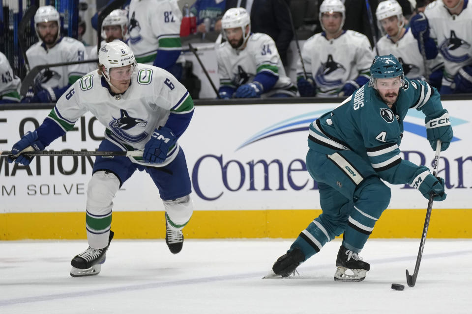 San Jose Sharks defenseman Kyle Burroughs (4) passes the puck next to Vancouver Canucks right wing Brock Boeser (6) during the second period of an NHL hockey game in San Jose, Calif., Saturday, Nov. 25, 2023. (AP Photo/Jeff Chiu)