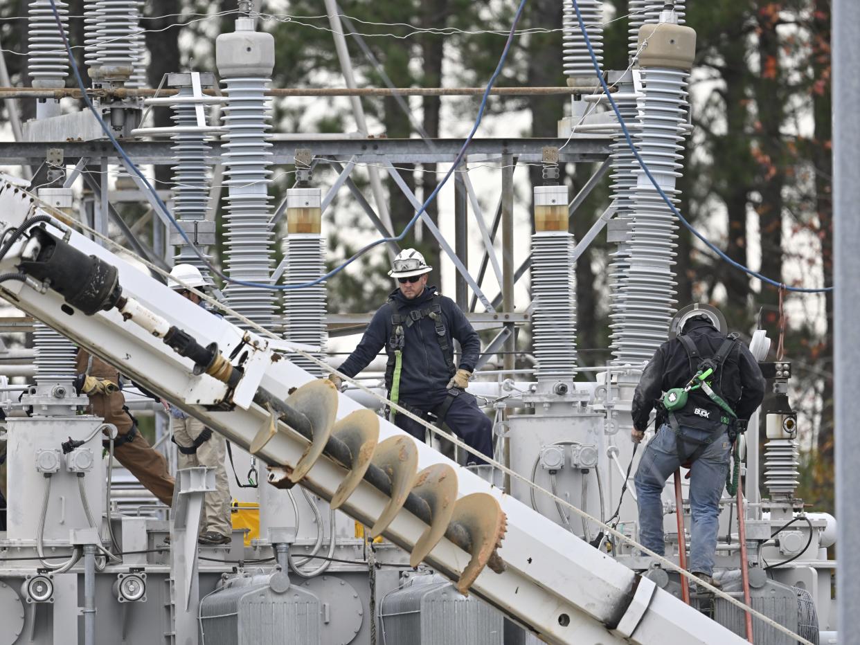 Workers stand amid electrical infrastructure.