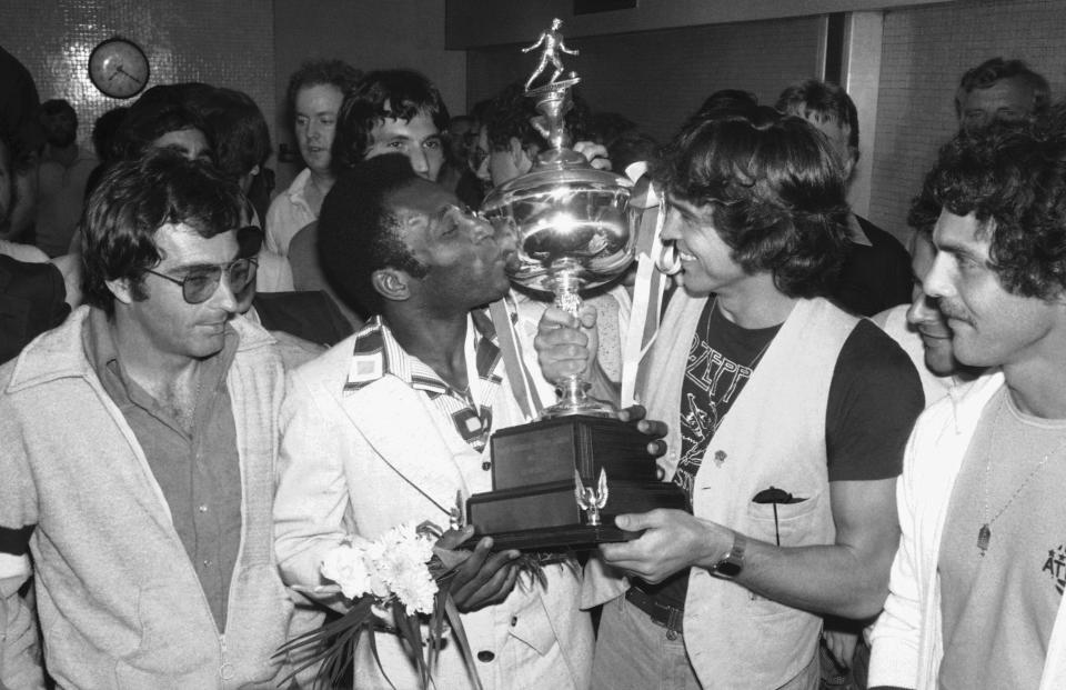 FILE - New York Cosmos' star Pele kisses a trophy held up by team captain Werner Roth at New York's Kennedy Airport on Aug. 29, 1977, as the team returned after winning the North American Soccer League Championship. Dozens of meetings over four years led to Pelé agreeing to sign with Cosmos in June 1975. His 2 1/2 seasons in New York elevated the sport, putting U.S. soccer on a path to hosting the World Cup in 1994 and launching Major League Soccer two years later. (AP Photo, File)