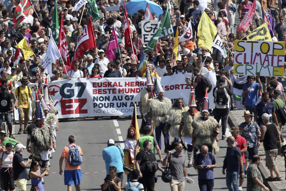 A group of Basque Joaldunak, cowbell wearers dressed in sheep fur, join anti-G-7 activists crossing a bridge from Hendaye, France, to Irun, Spain, during a protest Saturday, Aug. 24, 2019. World leaders and protesters are converging on the southern French resort town of Biarritz for the G-7 summit. President Donald Trump will join host French President Emmanuel Macron and the leaders of Britain, Germany, Japan, Canada and Italy for the annual summit in the nearby resort town of Biarritz. Banner in Basque, French and Spanish reads, "No to G7, Creating another world". (AP Photo/Bob Edme)