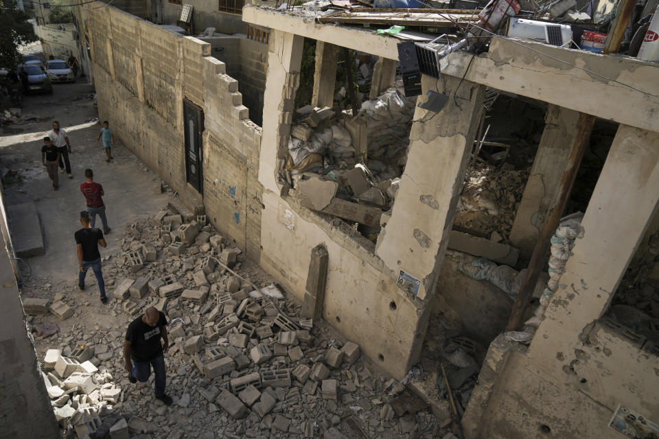 Palestinians walk by a damaged house in the Jenin refugee camp in the West Bank, Wednesday, July 5, 2023, after the Israeli army withdrew its forces from the militant stronghold. The withdrawal of troops from the camp ended an intense two-day operation that killed at least 13 Palestinians, drove thousands of people from their homes and left a wide swath of damage in its wake. One Israeli soldier was also killed. (AP Photo/Nasser Nasser)