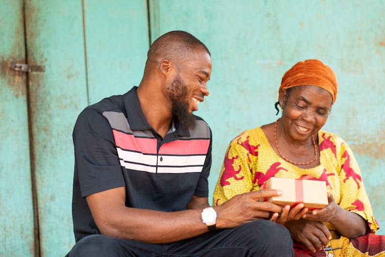 Young Black man smiling as he hands his grandmother a parcel.