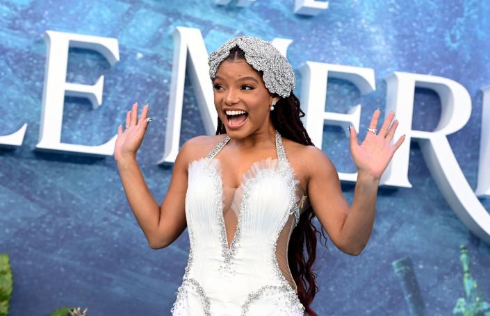 halle bailey smiling and waving with both hands at a film premiere