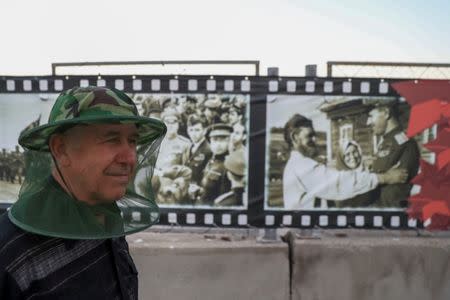 A man wears a mosquito head net as he stands next to World War II era pictures in the bank of Volga river in Volgograd, Russia, June 21, 2018. REUTERS/Sergio Perez