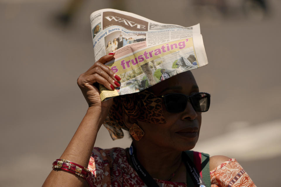 FILE - A woman shields herself from the sunlight with a copy of the Los Angeles Wave newspaper, July 15, 2023, in the Leimert Park neighborhood of Los Angeles. A historic heat wave that turned the Southwest into a blast furnace throughout July is beginning to abate with the late arrival of the monsoon rains. (AP Photo/Damian Dovarganes, File)