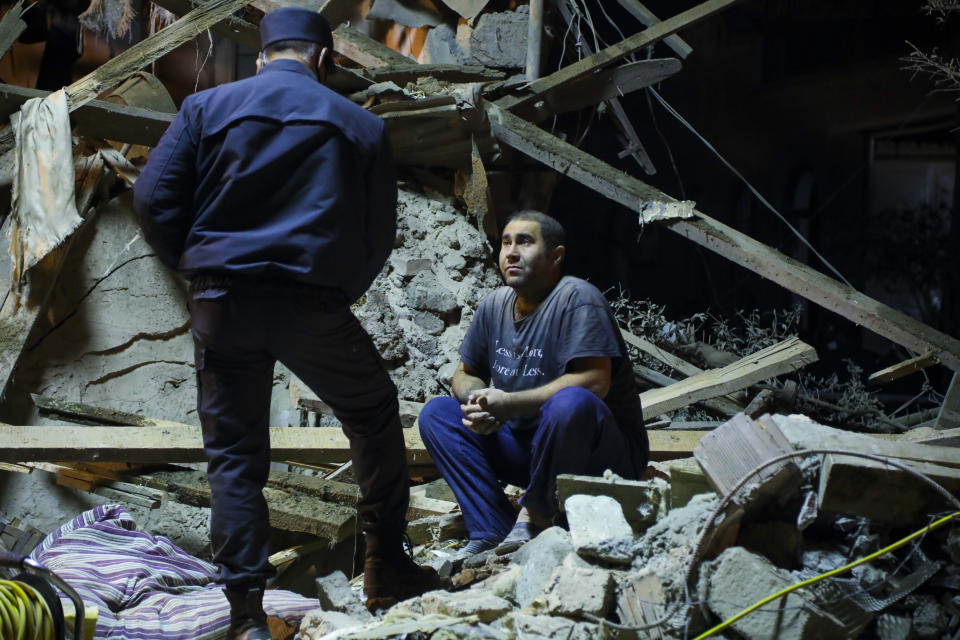 An Azerbaijan's policeman, left, speaks to a man siting at his destroyed house in a residential area that was hit by rocket fire overnight by Armenian forces, early Saturday, Oct. 17, 2020, in Ganja, Azerbaijan's second largest city, near the border with Armenia. (AP Photo/Aziz Karimov)
