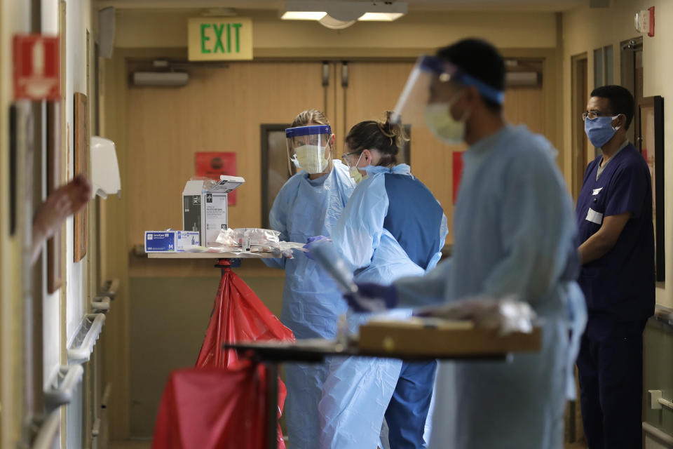 In this Friday, April 17, 2020, photo, members of a team of University of Washington medical providers work while conducting testing for the new coronavirus at Queen Anne Healthcare, a skilled nursing and rehabilitation facility in Seattle, as a worker from the facility looks on at right. Sending "drop teams" from University of Washington Medicine to conduct universal testing at skilled nursing facilities in collaboration with public health officials is one aspect of the region's approach to controlling the spread of the coronavirus. (AP Photo/Ted S. Warren)