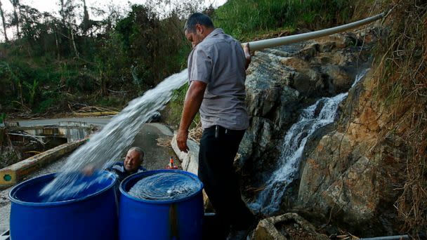 PHOTO: Luis Hernandez, left, gets help from Sergio Rivera, center, with filling drums with spring water for washing in Jayuya, Puerto Rico, the public water system isn't working full-time, so many collect water from the mountain springs, Oct. 4, 2017. (Carolyn Cole/Los Angeles Times via Getty Images)