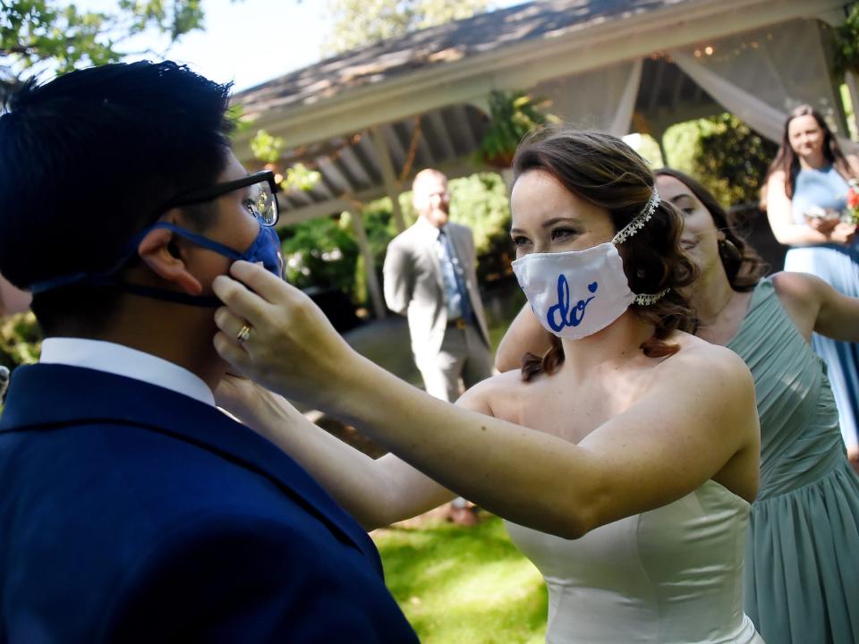 Bride wearing "I Do" face mask adjusts groom's matching mask at outdoor wedding