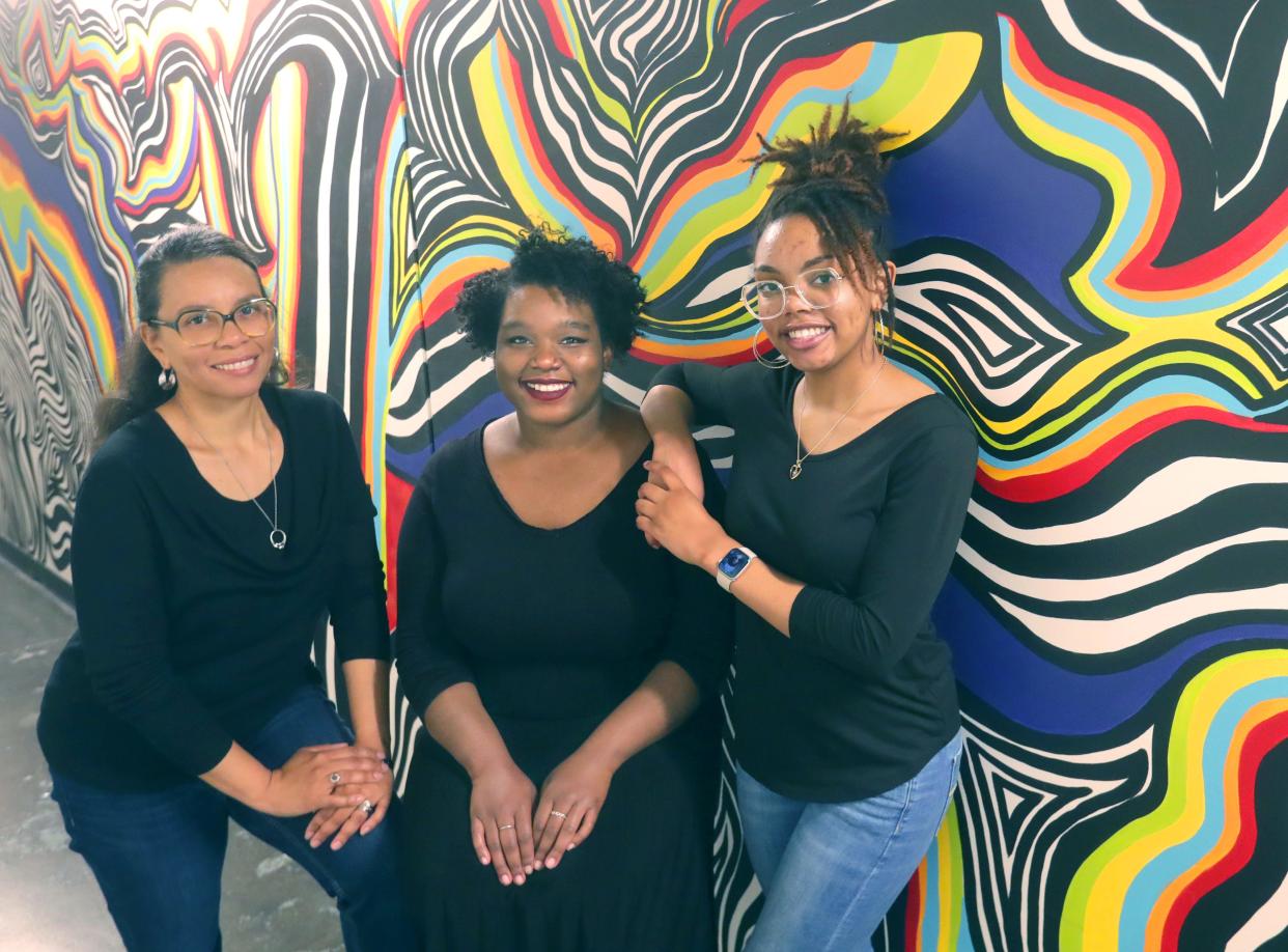 Artists Stephanie Stewart, Talia Hodge, and Kayla Stewart, pose for a photo in front of a mural at the Bounce Innovation Hub in Akron.