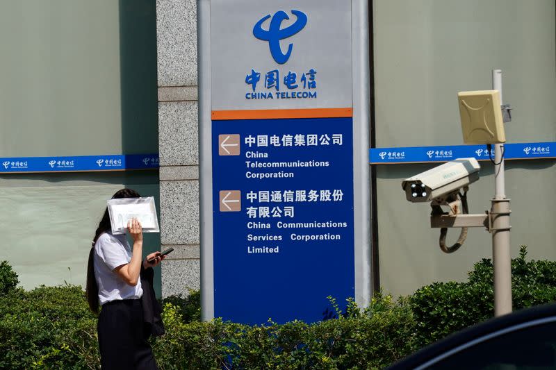 FILE PHOTO: Woman shields herself from the sun as she walks past an office building of China Telecom, in Beijing