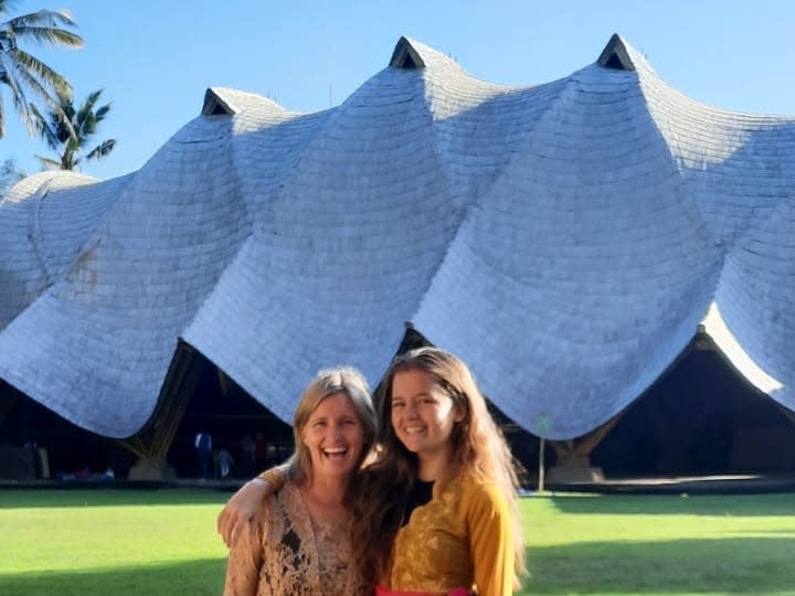 A woman and a young girl standing side by side in front of a bamboo school building in Bali.