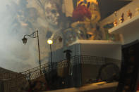 A man, reflected in a carnival masks shop display window, crosses a bridge at the Murano island in Venice, Italy, Monday, March 2, 2020. The Carnival period in Venice usually marks the start of peak season in one of the world's most visited cities, with hordes of tourists piling onto vaporettos to cruise the Grand Canal, strolling through cobble-stoned streets and lingering in picturesque cafes. Venice in the time of coronavirus, though, is a shell of itself, with empty piazzas, shuttered basilicas and gondoliers idling their days away. (AP Photo/Francisco Seco)